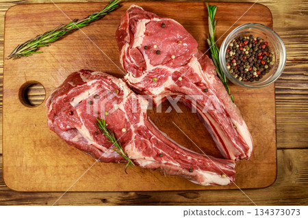 Raw fresh beef rib eye steaks on bone with spices and rosemary on wooden table. Top view 134373073