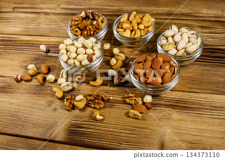 Assortment of nuts on wooden table. Almond, hazelnut, pistachio, walnut and cashew in glass bowls. Healthy eating concept 134373110