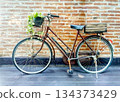 Vintage bicycle parked against a textured brick wall with plant 134373429