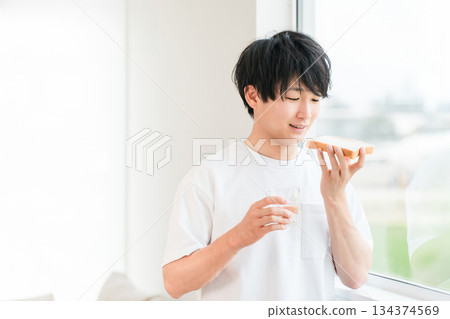 一位年輕的亞洲男子在他家窗邊吃麵包 134374569