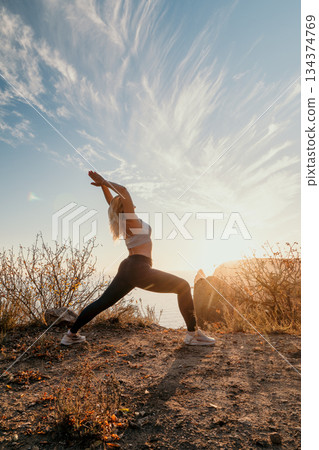 Yoga Woman Mountain Sunset Nature - A woman performs yoga in warrior pose on a mountaintop with a sunset backdrop. 134374769
