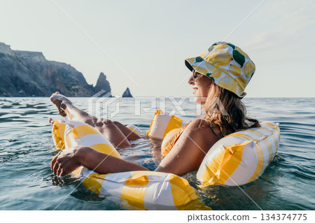 Woman, Beach, Inflatable, Relaxing on a Striped Inflatable Float in the Sea. 134374775