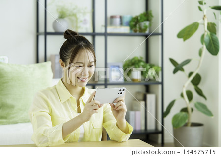 Portrait of a smiling Japanese woman watching videos on her smartphone in the living room Portrait of a smiling Japanese woman watching videos on her smartphone in the living room 134375715