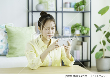 Portrait of a Japanese woman with a troubled face watching videos on her smartphone in the living room Portrait of a Japanese woman with a troubled face watching videos on her smartphone in the living room 134375720