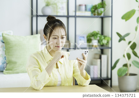 Portrait of a dissatisfied Japanese woman watching videos on her smartphone in the living room 134375721