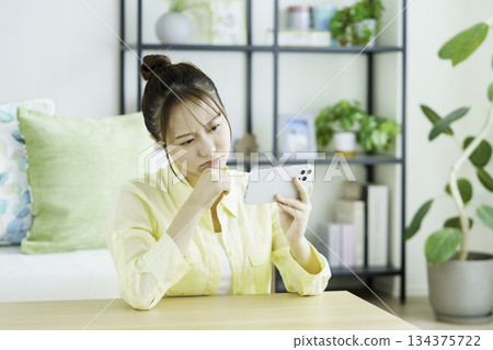 Portrait of a thinking Japanese woman watching videos on her smartphone in the living room 134375722