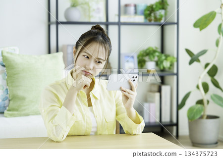 Portrait of a thinking Japanese woman watching videos on her smartphone in the living room 134375723