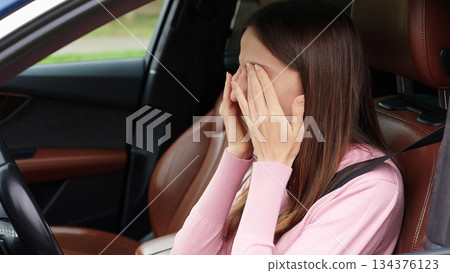Woman in car rubs her eyes, showing signs of fatigue, eye strain, or stress while sitting in the driver seat. 134376123