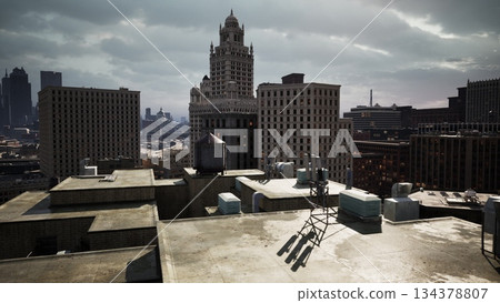 The sun peeks through clouds above a bustling city skyline. Old and new buildings contrast, showcasing historical architecture alongside modern structures. Antennas rise on rooftops. The sun peeks through clouds above a bustling city skyline. Old and new buildings contrast, showcasing historical architecture alongside modern structures. Antennas rise on rooftops. 134378807