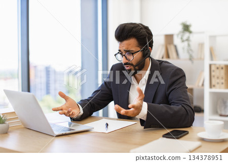 An Arab businessman gestures while participating in a video conference call using a headset and laptop 134378951