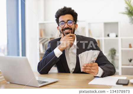 An Indian businessman smiles while holding a wad of cash, looking pleased with his financial success An Indian businessman smiles while holding a wad of cash, looking pleased with his financial success 134378973