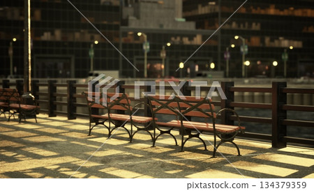 A serene waterfront lined with wooden benches creates a peaceful atmosphere. Warm light casts long shadows on the pavement, inviting visitors to relax and enjoy the view. 134379359