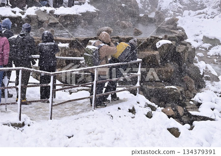 A person taking a photo of Japanese macaques bathing in the hot springs at Jigokudani Monkey Park in winter A person taking a photo of Japanese macaques bathing in the hot springs at Jigokudani Monkey Park in winter 134379391