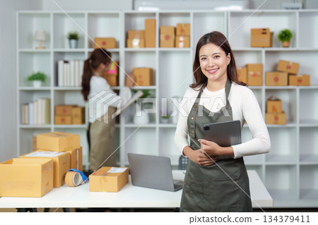 E-commerce workspace. Smiling woman in apron holding tablet in a retail environment. 134379411