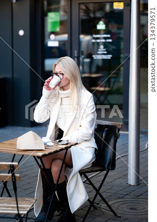 Sipping coffee at a cozy outdoor cafe while enjoying a serene moment in a bustling city setting during the afternoon sun's gentle warmth 134379571