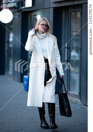 Elegant woman strolling in winter attire, showcasing fashion-forward style on a city street during a crisp afternoon Elegant woman strolling in winter attire, showcasing fashion-forward style on a city street during a crisp afternoon 134379574