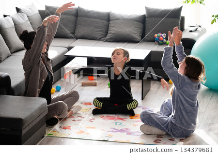 Children engage in mindful stretching exercises in a cozy living room filled with colorful toys and a large exercise ball during a sunny afternoon Children engage in mindful stretching exercises in a cozy living room filled with colorful toys and a large exercise ball during a sunny afternoon 134379681