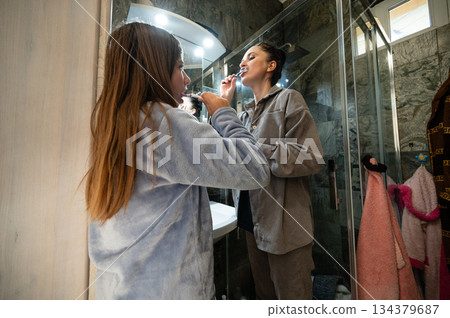 Morning routine unfolds in a cozy bathroom as a young girl brushes her teeth while her mother enjoys self-care time, creating a nurturing bonding moment before the day begins Morning routine unfolds in a cozy bathroom as a young girl brushes her teeth while her mother enjoys self-care time, creating a nurturing bonding moment before the day begins 134379687
