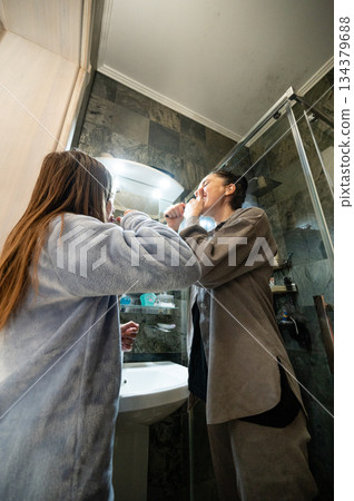 Together in the morning routine, two friends share moments while brushing teeth in a cozy bathroom filled with natural light and warmth during the early hours of the day Together in the morning routine, two friends share moments while brushing teeth in a cozy bathroom filled with natural light and warmth during the early hours of the day 134379688