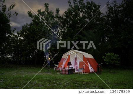 Camping tents at night, vintage cabin tents, antique oil lamps, retro chairs, and a group of camping tents with outdoor coffee-making facilities on wooden tables in a forest camping area. Camping tents at night, vintage cabin tents, antique oil lamps, retro chairs, and a group of camping tents with outdoor coffee-making facilities on wooden tables in a forest camping area. 134379869