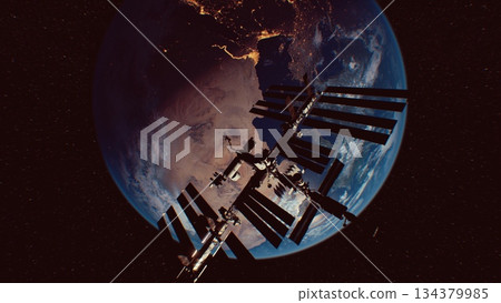 Suspended in space, the International Space Station glows as it orbits Earth. The planet shines below, highlighting city lights and the curvature of the atmosphere in a stunning night scene. 134379985