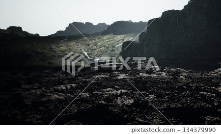 Misty morning light softly illuminates rugged cliffs and a rocky terrain in a tranquil highland valley. Gentle streams weave through the landscape, creating a serene atmosphere. 134379990