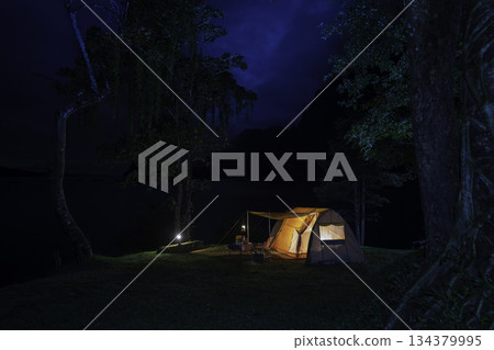 Night camping adventure with a cozy tent lit under the starry sky in a summer forest Night camping adventure with a cozy tent lit under the starry sky in a summer forest 134379995