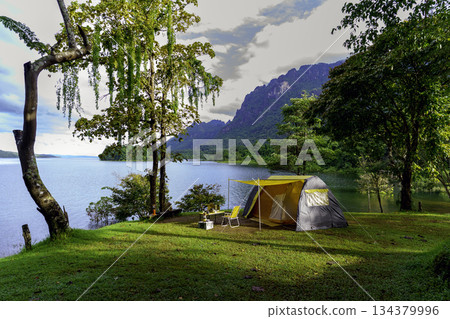 Camping tent on green grass in the morning, antique gas lamps, retro chairs, with outdoor coffee-making facilities on tables in a forest camping area. Camping tent on green grass in the morning, antique gas lamps, retro chairs, with outdoor coffee-making facilities on tables in a forest camping area. 134379996