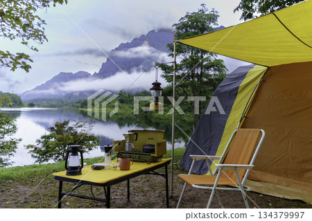Camping tents in the morning, vintage cabin tents, antique oil lamps, retro chairs, and a group of camping tents with outdoor coffee-making facilities on wooden tables in a forest camping area. Camping tents in the morning, vintage cabin tents, antique oil lamps, retro chairs, and a group of camping tents with outdoor coffee-making facilities on wooden tables in a forest camping area. 134379997