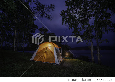Night camping adventure with a cozy tent lit under the starry sky in a summer forest Night camping adventure with a cozy tent lit under the starry sky in a summer forest 134379998