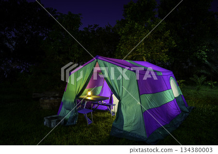 Nighttime camping tent in a forest clearing surrounded by nature 134380003