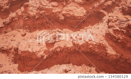 Vivid red rock formations create intricate patterns on the ground. The warm hues of sunset enhance the natural beauty of the landscape. A sense of calmness fills the air. 134380129