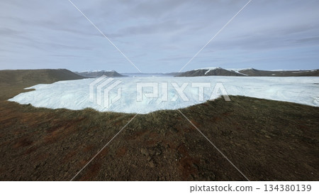 A breathtaking scene shows a vast glacier extending over rocky ground in Iceland. The icy blue surface contrasts beautifully with the earthy tones of the landscape. 134380139