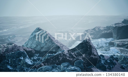 A rugged landscape features sharp, icy rocks amidst a serene, misty atmosphere. Twilight casts a soft glow, revealing shadows and textures on the rocky terrain. A rugged landscape features sharp, icy rocks amidst a serene, misty atmosphere. Twilight casts a soft glow, revealing shadows and textures on the rocky terrain. 134380148
