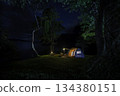 Night camping adventure with a cozy tent lit under the starry sky in a summer forest 134380151
