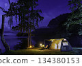 Night camping adventure with a cozy tent lit under the starry sky in a summer forest 134380153