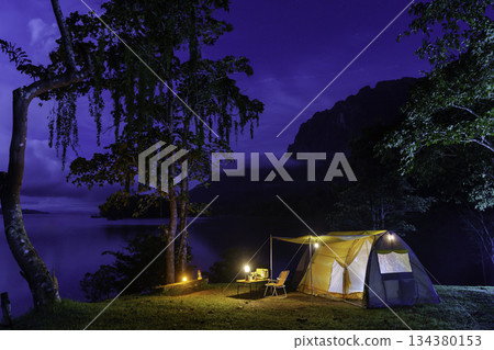 Night camping adventure with a cozy tent lit under the starry sky in a summer forest 134380153