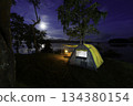 Night camping adventure with a cozy tent lit under the starry sky in a summer forest 134380154