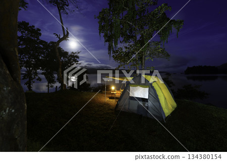 Night camping adventure with a cozy tent lit under the starry sky in a summer forest 134380154