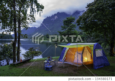 Camping tent on green grass in the morning, antique gas lamps, retro chairs, with outdoor coffee-making facilities on tables in a forest camping area. 134380171