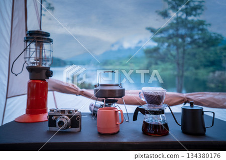 Coffee drip set for camping inside a tent, looking out to the mountain and lake view. 134380176