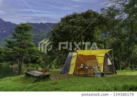 Camping tent on green grass in the morning, antique gas lamps, retro chairs, with outdoor coffee-making facilities on tables in a forest camping area. 134380179