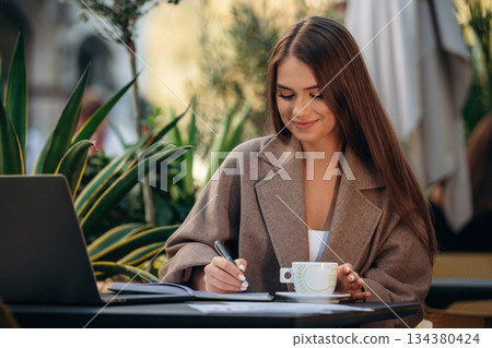Business deals, with laptop and pen. Beautiful young woman is outdoors of the restaurant by the table 134380424
