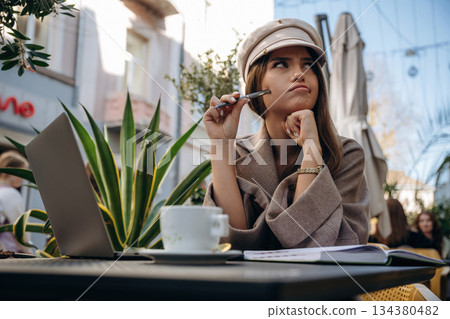 Writer is with pen. Beautiful young woman is outdoors of the restaurant by the table Writer is with pen. Beautiful young woman is outdoors of the restaurant by the table 134380482