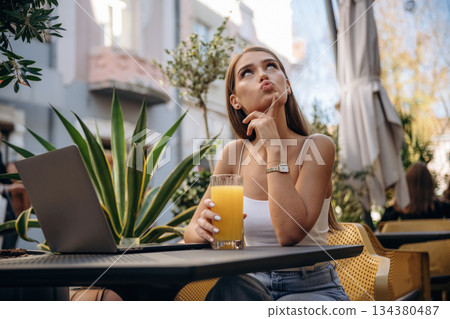 Orange juice drink. Beautiful young woman is outdoors of the restaurant by the table Orange juice drink. Beautiful young woman is outdoors of the restaurant by the table 134380487
