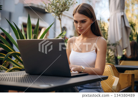Working with laptop. Beautiful young woman is outdoors of the restaurant by the table Working with laptop. Beautiful young woman is outdoors of the restaurant by the table 134380489