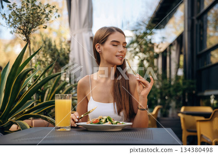 Delicious food. Beautiful young woman is outdoors of the restaurant by the table Delicious food. Beautiful young woman is outdoors of the restaurant by the table 134380498