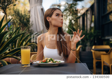 Delicious food. Beautiful young woman is outdoors of the restaurant by the table Delicious food. Beautiful young woman is outdoors of the restaurant by the table 134380500