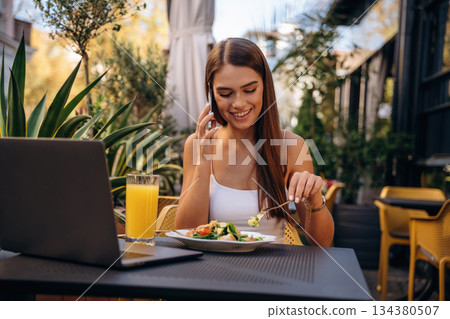 Talking by phone. Beautiful young woman is outdoors of the restaurant by the table 134380507