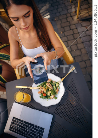 Making a photo of food. Beautiful young woman is outdoors of the restaurant by the table Making a photo of food. Beautiful young woman is outdoors of the restaurant by the table 134380513
